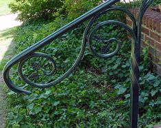 an iron railing next to a brick wall and green plants on the side of it