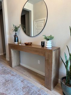 a wooden table sitting in front of a mirror next to a potted plant on top of a rug