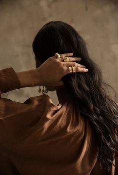 a woman with long hair wearing gold rings on her left hand and holding the back of her head