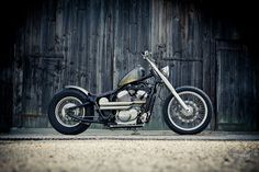 a black motorcycle parked in front of a wooden building with a barn door behind it