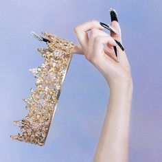 a woman's hand holding up a gold tiara with black and white nails