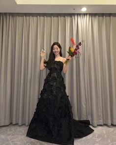 a woman in a black dress holding flowers and posing for the camera with her hands up