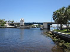 there is a bridge over the water with palm trees on both sides and a clock tower in the distance