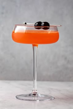 an orange cocktail with two olives in it