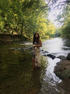 a woman standing in the middle of a river with her arms around her waist and head