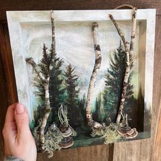 a person holding up a painting with trees in the background and moss growing on it