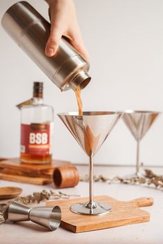 someone pouring something into a martini glass on top of a cutting board next to other items