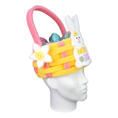 a white mannequin head wearing a yellow and pink basket filled with eggs, flowers and bunny ears