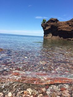 the water is crystal clear and there are rocks on the shore near the rock outcropping