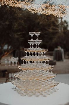 a tall glass cake sitting on top of a white table covered in wine goblets