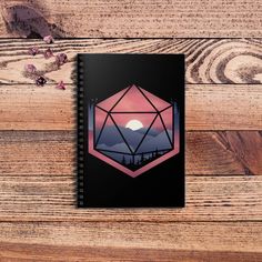 a spiral notebook with an image of mountains and trees on the cover, sitting on a wooden surface