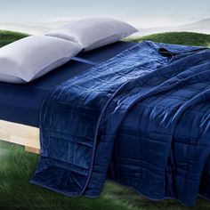 an image of a bed with blue sheets and white pillows on it in the grass