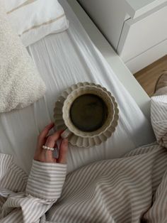 a woman laying in bed holding a coffee cup with her hands on the edge of it