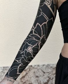 a woman's arm with black and white tattoos on her left arm, in front of a wall