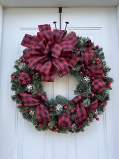 a christmas wreath hanging on the front door with red and black plaid bow, holly berry berries and snowflakes