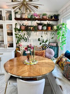 a dining room table with white chairs and plants on the wall