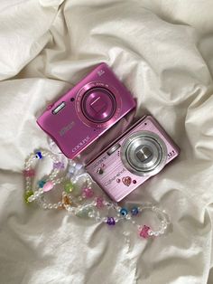 a pink camera sitting on top of a bed next to a beaded bracelet and necklace