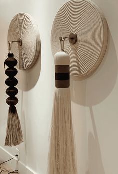 two wall hangings with tassels on them in a white walled room next to each other