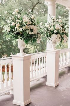 two vases filled with white flowers sitting on top of a porch