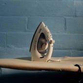 an ironing board with a white electric iron on it next to a blue brick wall