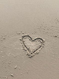 a heart drawn in the sand with water droplets on it's sides and bottom