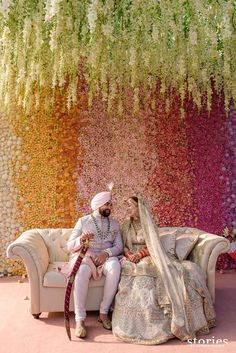 a bride and groom sitting on a couch in front of a rainbow colored backdrop with flowers