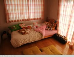 a bed with stuffed animals on it in a bedroom next to two windows and wooden floors