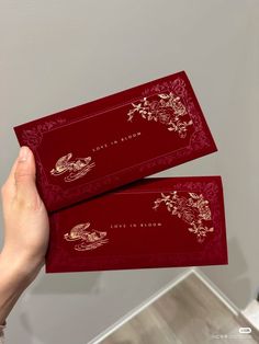 two red envelopes with gold foil designs on the front and back, held up by a person's hand