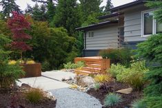 a wooden bench sitting in the middle of a garden next to a house and trees