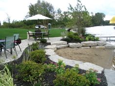 a patio area with tables, chairs and an umbrella next to the water's edge