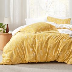 a bed with yellow comforter and pillows in a room next to a lamp on the floor