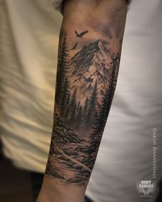 a man's arm with a mountain scene and trees on the back of it