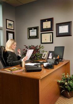 a woman sitting at a desk in front of a window with pictures on the wall