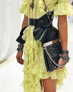 a woman in a yellow dress holding a black purse on the catwalk at a fashion show