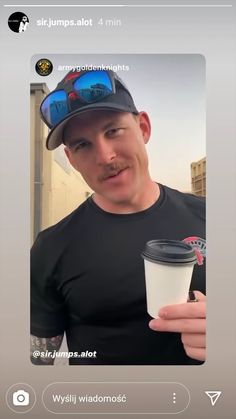 a man with a mustache holding a coffee cup and looking at the camera while wearing a baseball cap