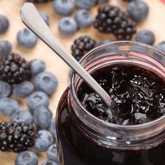 a glass jar filled with blueberries next to some berries on a cutting board and spoon