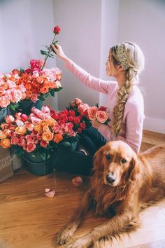 a woman sitting on the floor next to a large bouquet of flowers and a dog