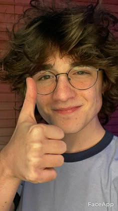 a young man wearing glasses giving the thumbs up sign