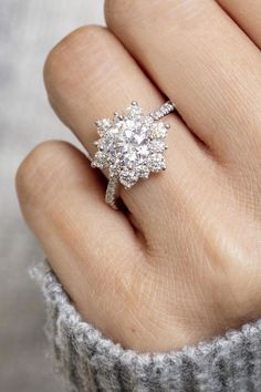 a woman's hand with a diamond ring on top of her finger, in front of a gray sweater