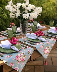 the table is set with pink and white flowers in vases, plates and napkins