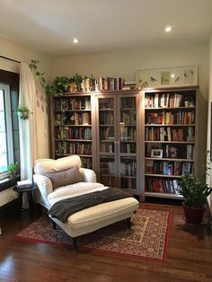 a living room filled with furniture and a book shelf next to a window on top of a hard wood floor