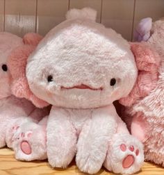 three pink stuffed animals sitting next to each other on a wooden floor in front of a wall