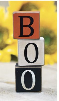 wooden blocks spelling the word b o on top of each other with sunflowers in the background