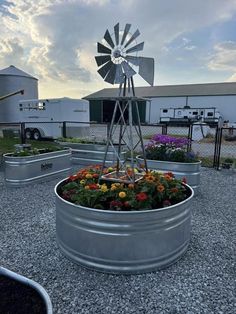 a large metal planter filled with flowers next to a farm house and silo