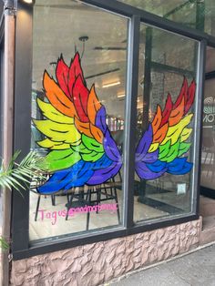 a storefront with colorful wings painted on the windows and in front of it is a plant