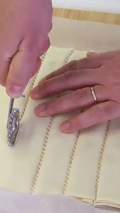 two hands are working on a piece of paper with a small metal object in the middle