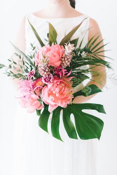 a woman in a white dress holding a bouquet of pink flowers and greenery on her arm