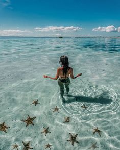 a woman is sitting in the water surrounded by starfish and looking at the ocean