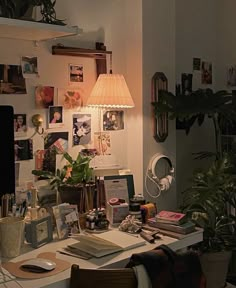 a cluttered home office with plants and pictures on the wall, including a desk lamp