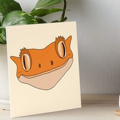 an orange and white gecko face on a beige background art boarder next to a potted plant